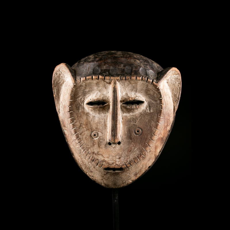 Front view of a Lega mask featuring large ears, narrow eyes and a light patina.