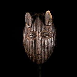 Front view of a Metoko wooden african mask with vertical carved grooves displayed on its custom metal stand.