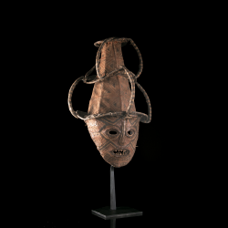 Vue de trois quarts du masque Makishi montrant le visage croûteux, les dents et l’armature de la coiffe.