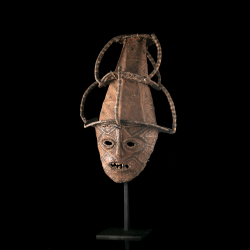 Masque Luchazi de Zambie présenté sur socle, décoré de motifs géométriques brun rouge.