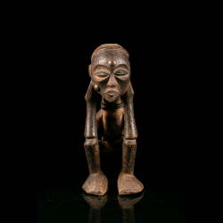 Front view of a Chokwe figure decorated with beads and rounded metal elements.