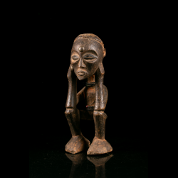 Crouching Chokwe wooden figure with both hands framing the face.