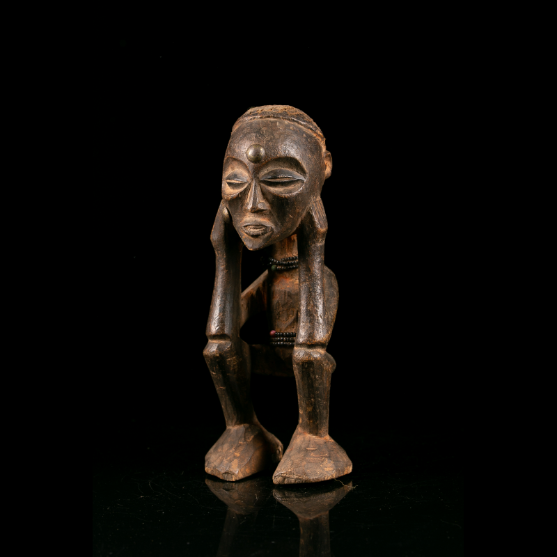 Crouching Chokwe wooden figure with both hands framing the face.
