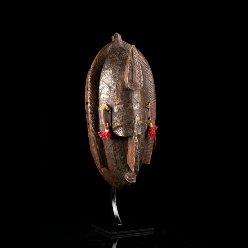 Vue de trois-quarts d'un masque Marka en bois et métal avec oreilles sculptées et ornements suspendus.
