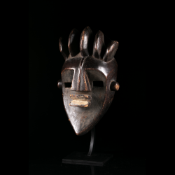 Masque africain Lwalwa Mfondo vu de trois quarts, montrant la géométrie du visage et la profonde patine sombre.