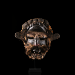 Vue frontale d’un masque Wè Guéré aux yeux profonds, moustache et crocs saillants.