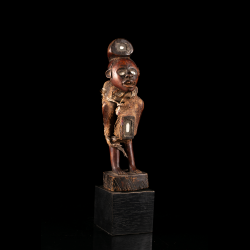 Vue de trois quarts du nkisi Kongo avec réceptacle abdominal, textile, fibres et patine brun rouge.