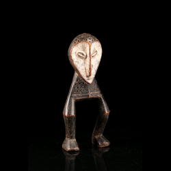 Vue latérale d’une figure Lega du Bwami montrant les longues jambes arquées et le visage recouvert de pigment blanc.