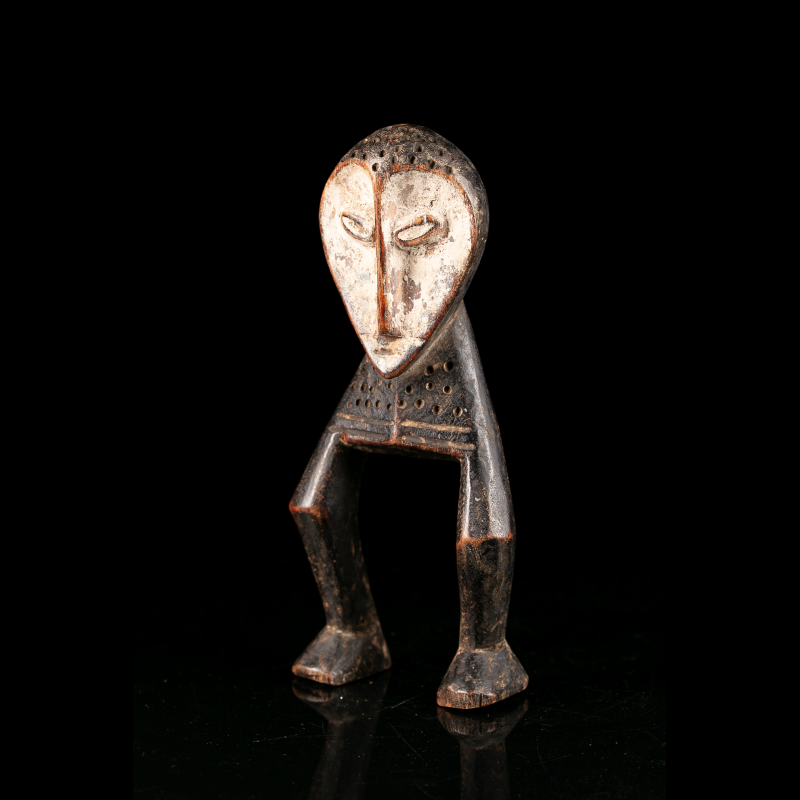 Vue de trois quarts d’une sculpture Lega Katanda en bois sculpté et pigment clair, associée au Bwami.